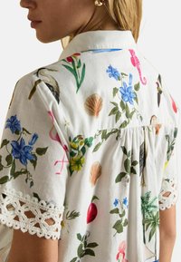 Floral printed shirt with a white background, featuring colorful birds, flowers, and seashells. Includes lace accents on the sleeves.
