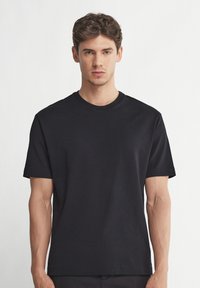 Svart T-shirt med kort ärm, tillverkad av mjuk bomull. Har rund halsringning och en avslappnad passform. Enfärgad utan mönster eller detaljer.