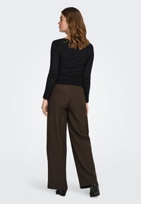 Schwarzes, geripptes Langarmoberteil kombiniert mit braunen, weit geschnittenen Hosen mit entspannter Passform und Gesäßtaschen, seitlich-rückwärtige Ansicht.