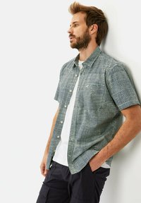 Korte mouwen overhemd met een geruit patroon in donkergroen en wit. Gemaakt van lichtgewicht stof. Gedragen over een eenvoudig wit T-shirt.