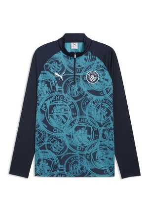 Top de entrenamiento de fútbol del Manchester City de manga larga en azul marino y azul, con medio cierre y patrones repetidos del escudo del club en el frente.