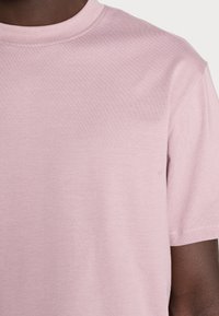 T-shirt rose clair à manches courtes, en tissu doux, avec un col rond simple et une texture lisse. Détails de couture le long des bords.