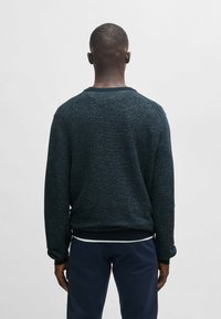 Dunkelblauer Sweatshirt mit Struktur, Rundhalsausschnitt und gerippten Bündchen, das ein dezentes Muster und eine lockere Passform aufweist. Rückansicht, kombiniert mit dunklen Hosen.