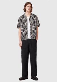 Chemise à manches courtes noire et blanche avec motif de fougère, portée sur un T-shirt blanc. Associée à un pantalon cargo noir ample et des chaussures noires.