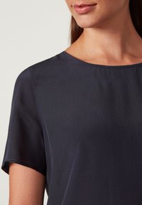 Mørkeblå silkebluse med korte ærmer, rund halsudskæring og en glat overflade. Har en subtil glans og en afslappet pasform.