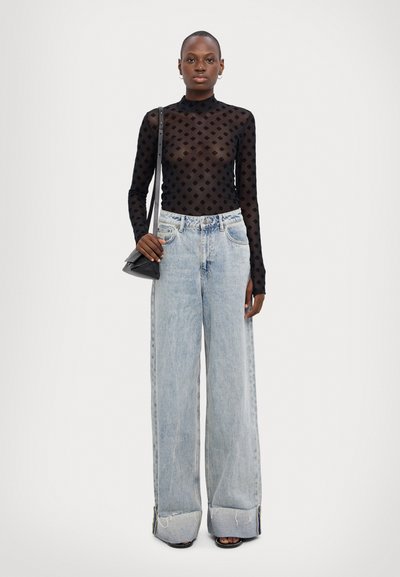 Top negro de malla de manga larga con un patrón de diamantes y cuello alto, combinado con pantalones vaqueros de pierna ancha de color azul claro. Detalle notable en el dobladillo deshilachado.
