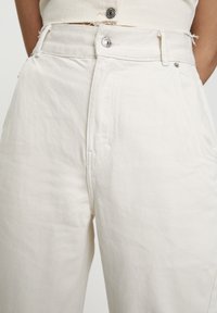 Pantalones de talle alto color crema con un diseño de pierna recta, elaborados en denim. Cuenta con trabillas para el cinturón, bolsillos frontales y un cierre de botón metálico.