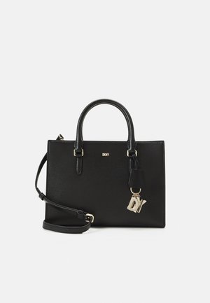 Sac à main structuré noir avec deux poignées, bandoulière amovible, logo DKNY et breloques en forme de lettres DV dorées suspendues à une poignée.