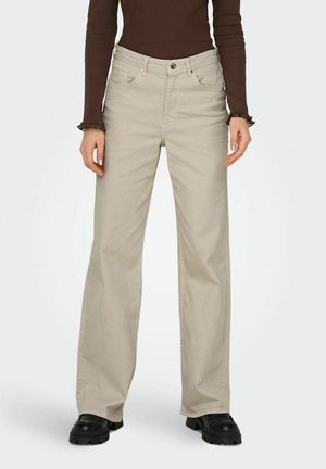 Pantalons beige à jambes droites en mélange de coton avec cinq poches, fermeture à bouton sur le devant et détails de couture visibles, associés à des bottes robustes noires.