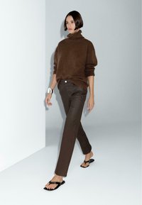 Brown turtleneck sweater paired with dark brown slim-fit pants and black flip-flops. Smooth texture throughout the outfit. Simple design.