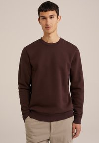 Felpa marrone scuro realizzata in morbido misto cotone, con scollatura rotonda e polsini a coste, abbinata a pantaloni chiari.
