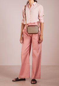 Tan-värinen olkalaukku, jossa on pyöreä kuvio. Laukku on yhdistetty vaaleanpunaiseen nappikauluspaitaan ja leveälahkeisiin vaaleanpunaisiin housuihin sekä mustiin liukusandaaleihin.