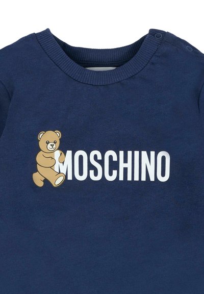 Granatowa koszula z logo Moschino, na którym znajduje się chodzący brązowy miś zintegrowany z białym tekstem na klatce piersiowej.