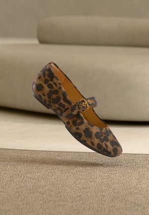 Brauner und schwarzer Leopardenmuster-Flachschuh mit goldener Schnallenriemen, auf beigem Teppich vor einem beigen Sofa platziert.