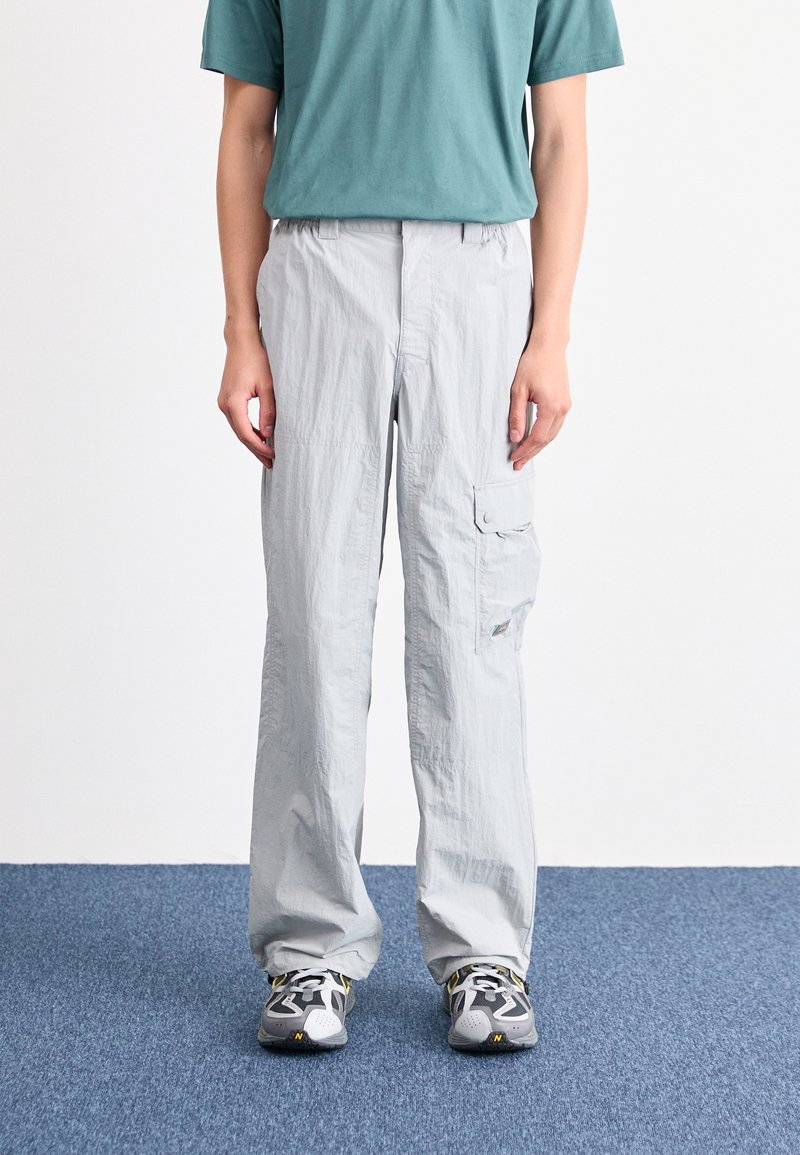 Pantalon cargo gris clair en tissu léger, doté d'une poche latérale, coupe ample et jambes droites, associé à des chaussures de sport grises.