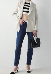Blazer blanc texturé, crop top rayé noir et blanc, jean bleu foncé, sac à main noir avec détail d'écharpe blanche et chaussures noires et blanches.