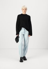 Crna oversized pletena majica, svijetloplave traperice, crna torba i masivni crni cipele; minimalistički dizajn s opuštenim krojem.