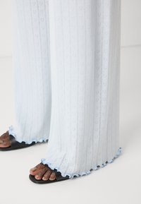 Helle blaue transparente Hosen mit Herzmustern, ausgestattet mit einem Rüschensaum in blauen Akzenten. Kombiniert mit schwarzen Flip-Flops.