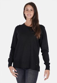 Maglione lungo nero a maniche lunghe con scollo rotondo, polsini a costine e orlo che si abbassa sul retro. Texture liscia, design minimalista.