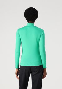 Green turtleneck sweater with a fitted design, ribbed texture, and scalloped hem and cuffs, paired with black pants.