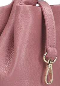 Details van een roze leren handtas: gestructureerd oppervlak, elegante rondingen, slanke schouderband en een glanzende goudkleurige sluiting.