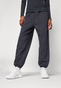 Dunkelgraue Sweatpants aus weichem Material, mit einem elastischen Bund und Bündchen, kombiniert mit weißen Sport Schuhen.