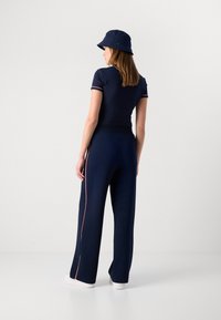 Dunkelblaues Outfit mit einem kurzärmeligen Top und weit geschnittenen Hosen mit einem roten Seitenstreifen. Kombiniert mit einem passenden dunkelblauen Bucket Hat.