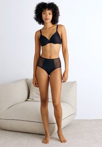 Schwarz(es) Lingerie-Set mit einem glatten BH mit verstellbaren Trägern und hochgeschnittenen Slips mit Netz-Seitenteilen. Enganliegendes und nahtloses Design.
