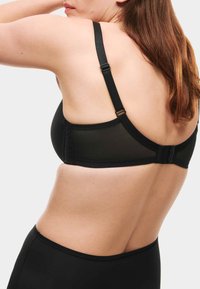 Sujeción negra con tela lisa, tirantes ajustables y cierre en la parte trasera. El diseño es sencillo, sin patrones ni adornos visibles.