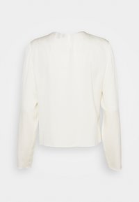 Blouse blanche à manches longues avec un col rond et un tissu uni et lisse vue de dos.