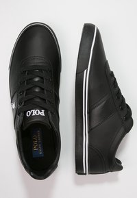 Svart lädersneakers med vita detaljer, med en rund tåkappa, platt snördesign och en logotyp på tungan. Slät yta genomgående.