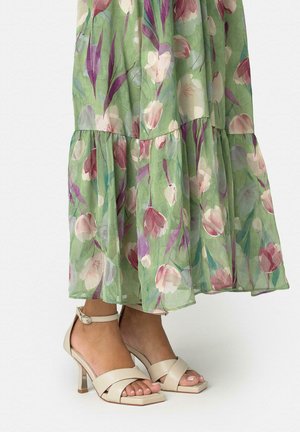 Sandalias beige de tacón alto con correas en el tobillo, combinadas con un vestido midi verde con flores rosas y moradas.