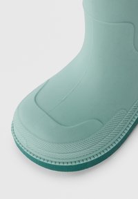 Botte en caoutchouc vert menthe avec un motif texturé, un corps lisse et une semelle robuste à crans. Bout arrondi et design à tige haute.