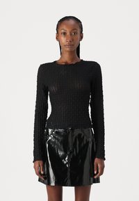 Black textured long-sleeve top with a fitted design, paired with a shiny black faux leather mini skirt featuring front pockets and a zipper.