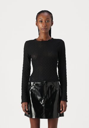 Black textured long-sleeve top with a fitted design, paired with a shiny black faux leather mini skirt featuring front pockets and a zipper.