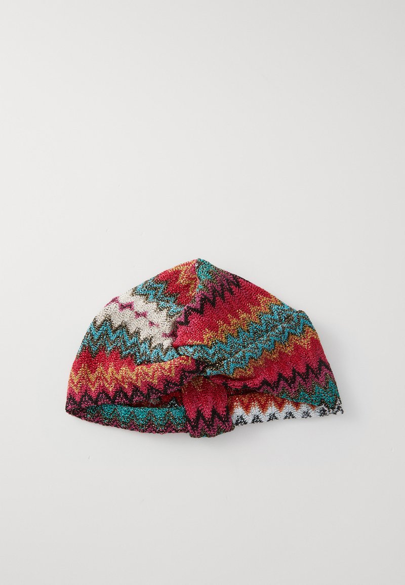 Căciulă tricotată multicoloră cu modele în zigzag roșu, teal, aurie și albă; are un bandaj legat în față.