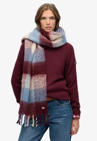 Bufanda de mezcla de lana con un patrón a cuadros en rojo, azul y crema, con bordes desflecados. Textura suave y gran tamaño para abrigar.