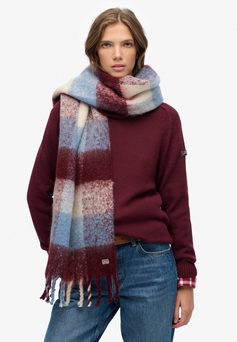 Bufanda de mezcla de lana con un patrón a cuadros en rojo, azul y crema, con bordes desflecados. Textura suave y gran tamaño para abrigar.
