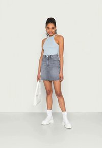 Top sem mangas azul claro, saia de ganga cinza com bainha desfiada, botas de combate brancas e uma mala branca. Design simples e moderno.