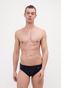 Caleçons de bain noirs avec des accents bleus, présentant une texture lisse et un design ajusté. Le logo de la marque est visible sur la ceinture.
