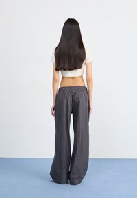Pantalones anchos de rayas grises y negras con cintura elástica, tela suave y corte relajado, combinados con una camiseta corta blanca.