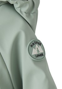 Light green waterproof jacket fabric with gathering detail at the sleeve, featuring a circular patch that reads "NATURE LOVER" with mountain design.