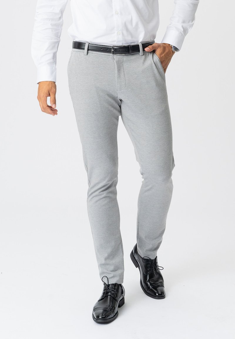 Grå slim-fit bukser lavet af blød stof, med forlommer og et sort bælte. Båret med skinnende sorte dress sko.