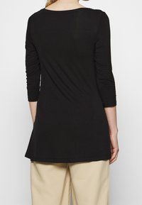 Svart långärmad topp med rundad halsringning, mjuk textur och avslappnad passform, med sammanknuten detalj längs ärmarna och en utsvängd nederkant.