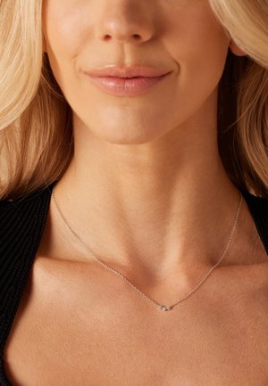 Collier en argent délicat avec de petites accents de cristal décoratifs, reposant sur un décolleté lisse sur fond de tissu noir.