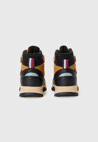 Zapatos de caña alta marrones y negros con forro de felpa, suelas de goma y una etiqueta trasera en rojo, blanco y azul. Presenta detalles metálicos.