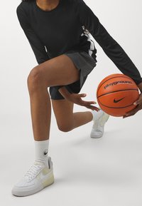 Camiseta negra de manga larga, pantalones cortos grises texturizados, zapatillas Nike Air Force 1 blancas, balón de baloncesto naranja y calcetines blancos con logo.