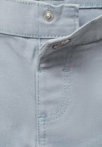 Țesătură de denim albastru deschis cu un sistem de închidere cu buton vizibil și detalii de cusătură. Are conturul unui buzunar și o textură netedă.