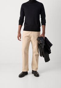 Pull en maille noir, pantalon beige à jambes droites, veste en cuir noire et bottines lisses. Design minimaliste avec une palette de couleurs neutres.