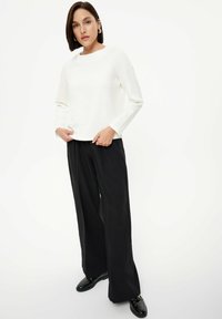 Witte textuur long-sleeve top gecombineerd met zwarte wijde broek en zwarte schoenen. De outfit heeft een ontspannen pasvorm en een minimalistisch ontwerp.